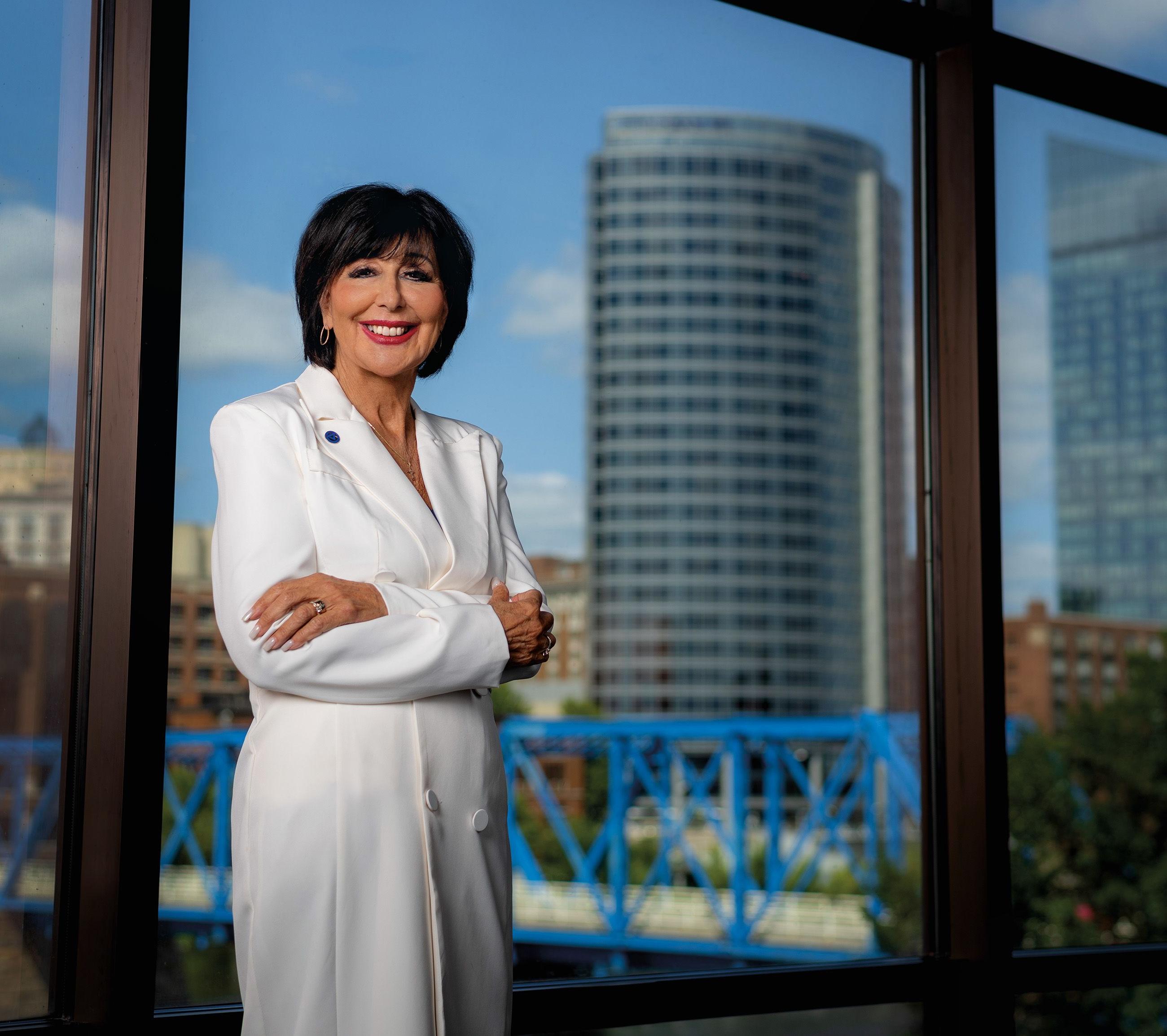 President Mantella in white jacket against window showing skyline of Grand Rapids