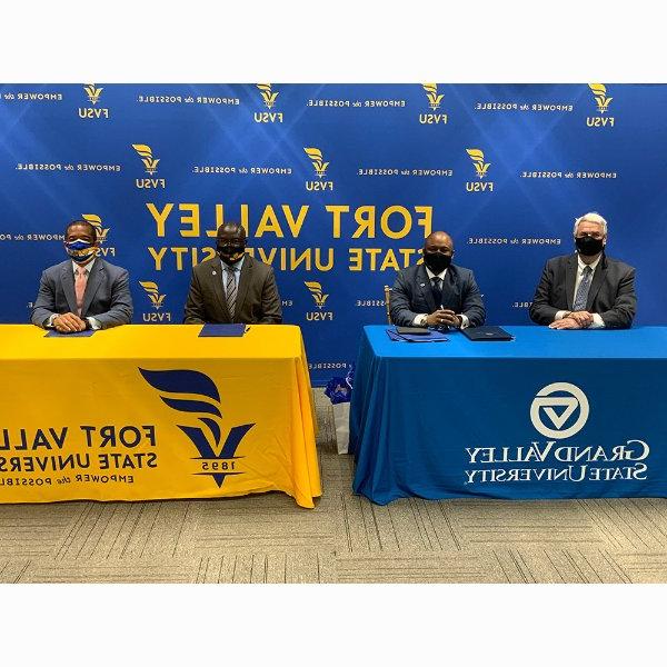 four people in masks seated at tables in front of sign at Fort Valley State University.