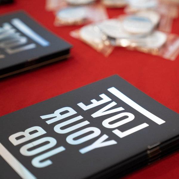 notebooks that read Love Your Job on a red tablecloth with white pins in plastic near the top