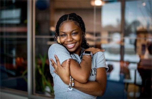 A portrait of a college student as she wraps her arms around herself smiling at the camera. 