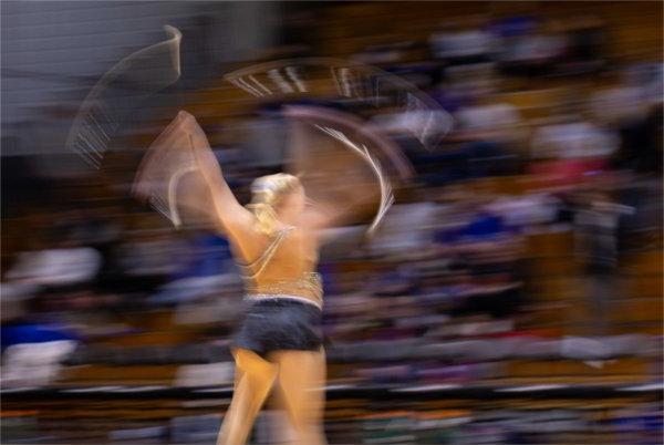 A blurred photo of a baton twirler in action in front of an audience. 