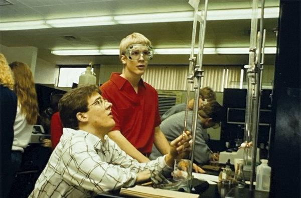 Two people, one wearing goggles, inspect an apparatus.