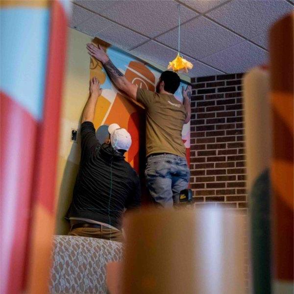 An installation worker places a strip of vinyl mural on the wall.