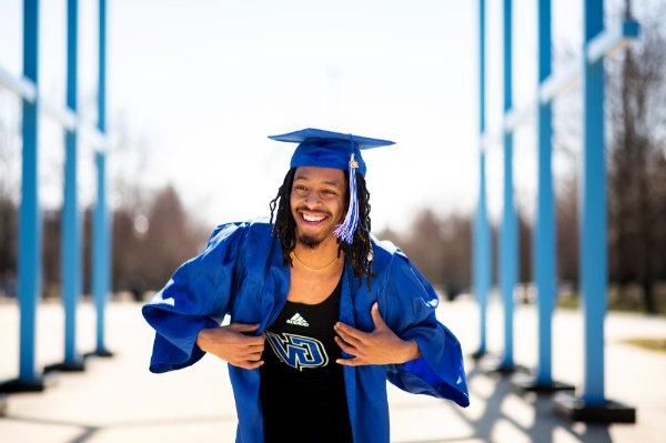 A person wearing a cap and gown smiles while showing a top with the words "adidas" and the initials "GV" on a shirt.