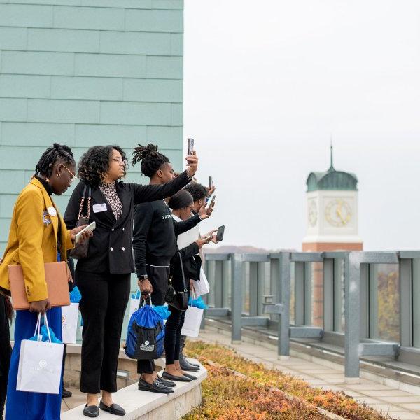 students stand on fourth floor balcony of Pew Library and take cell phone photos