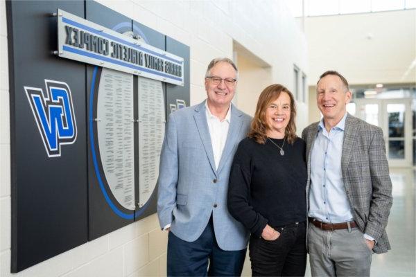 three people standing near hall of fame wall with names on plague in the Fieldhouse