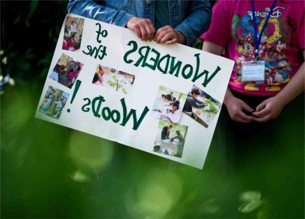 A teacher holds a sign showing off their student project "Wonders of the Woods!" during the Groundswell Stewardship Initiative student project showcase on the Pew Grand Rapids Campus May 15.