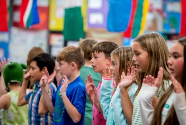  Middle-school aged children stand in a line with the palm of their hands facing out. Many colorful flags and posters hang behind them. 