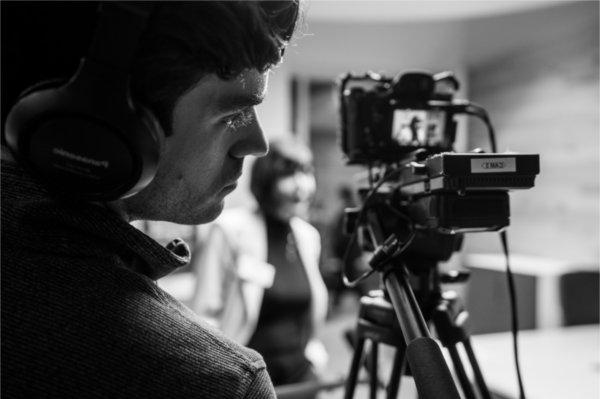 Close up photo of a person's face while they are operating a video camera. 