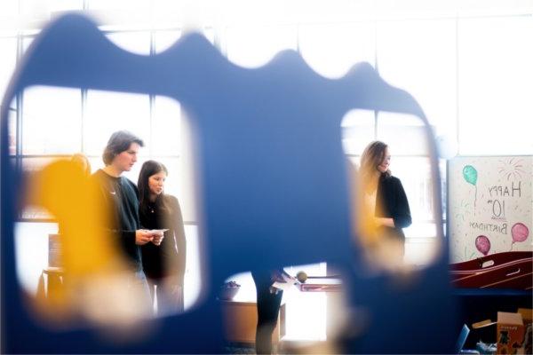 People, seen through openings of a poster board sign, participate in games. 