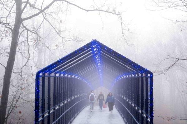 Pedestrians walk on a blue bridge in the fog. 