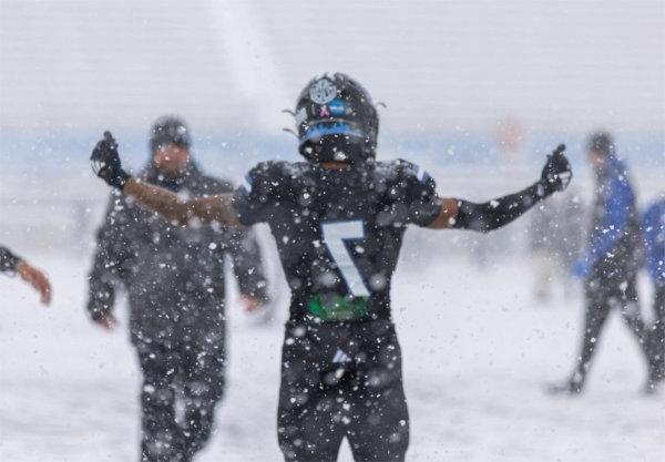 A football player holds up his hands during heavy snowfall. 