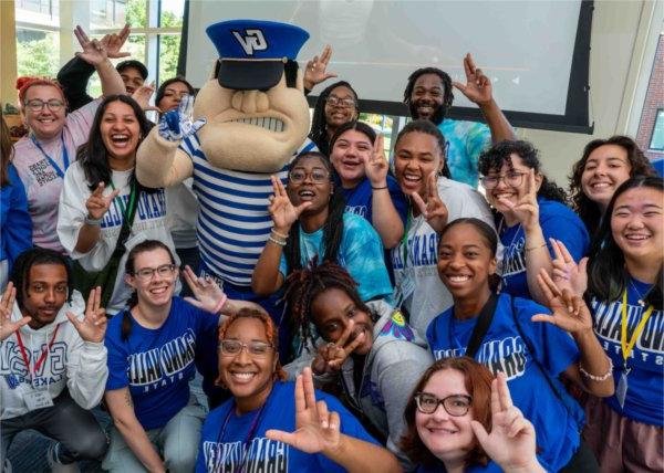  Students hold up a college hand signal as they surround the mascot.