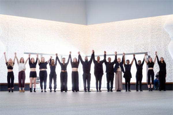 Holding hands with their arms raised a long line of performers share a curtain call together.