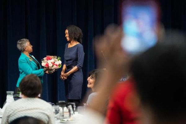 A woman is being presented with a bouquet of flowers at the front of a full room. 