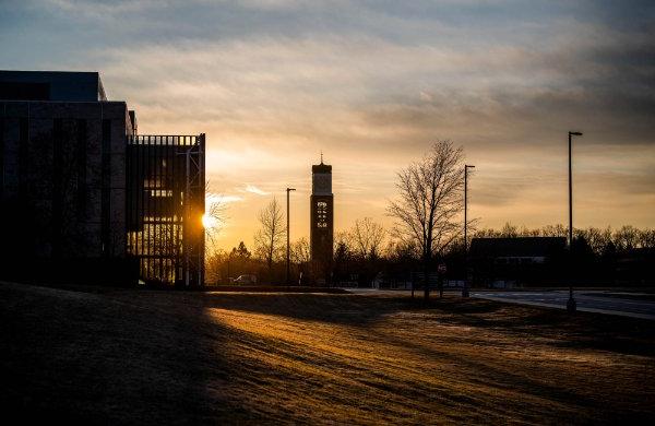 The sunrise illuminates a carillon tower and library building on a college campus.