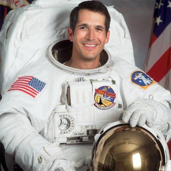 A person wearing an astronaut uniform smiles.