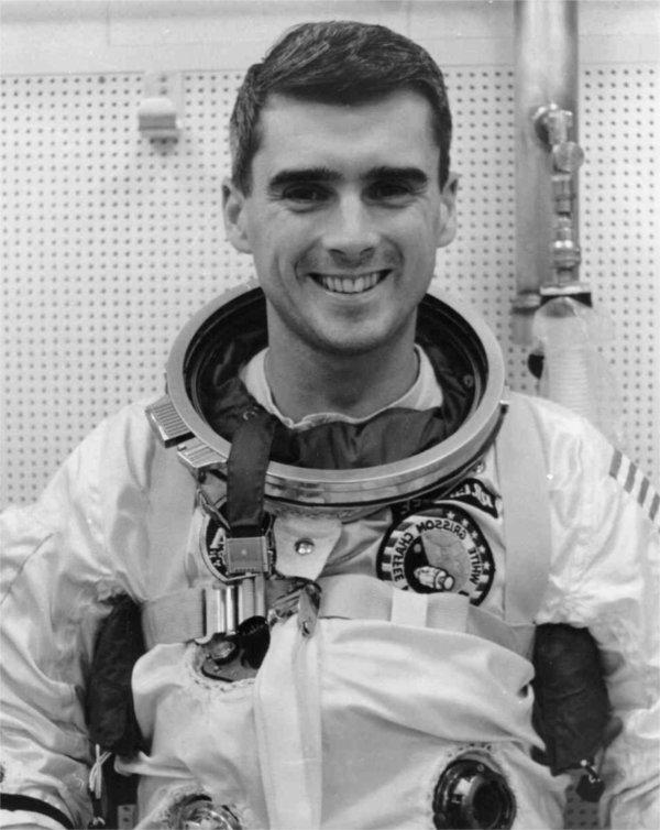 A person wearing an astronaut uniform smiles in a black and white photo.