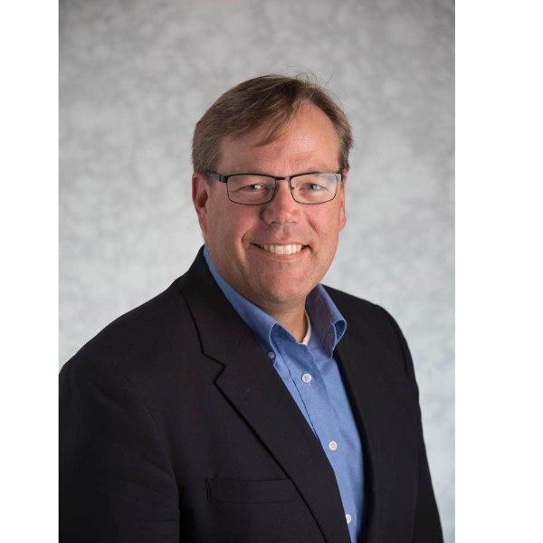 Greg Warsen headshot, he is wearing a dark jacket and blue shirt