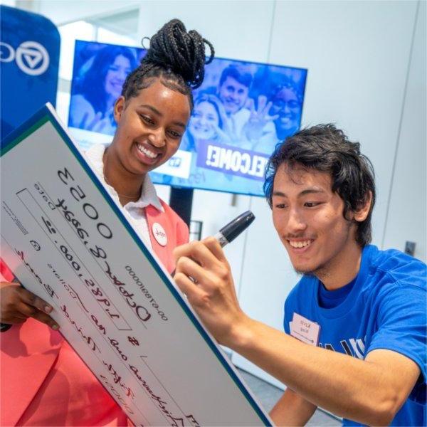 Two GVSU students smile and sign an oversized check made out to Grand Valley State University.