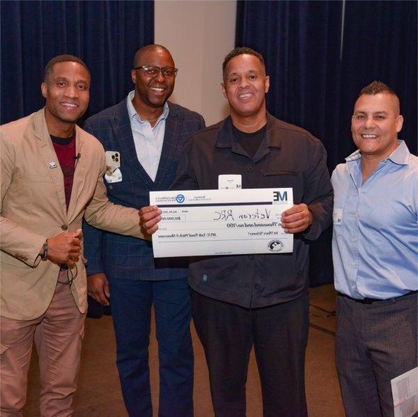 four people standing in row, two in center holding oversized check