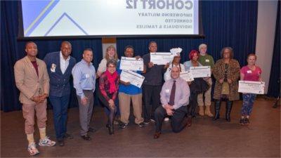 large group of people standing, some holding oversized check