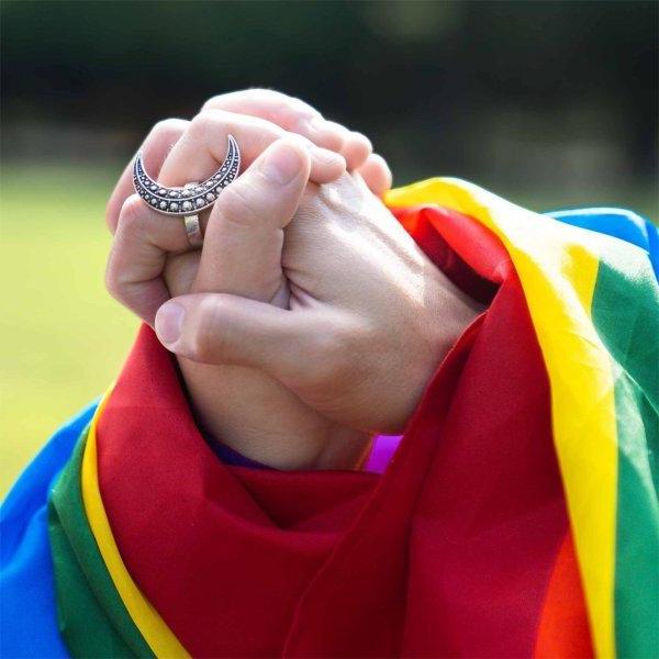 Two folded hands draped with a rainbow pride flag.