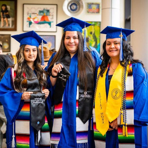 three women in blue graduation gowns and Latino stoles