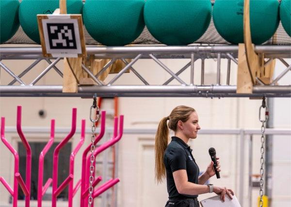 Avery Schuen with microphone above her a row of green exercise balls, pink coral to the right