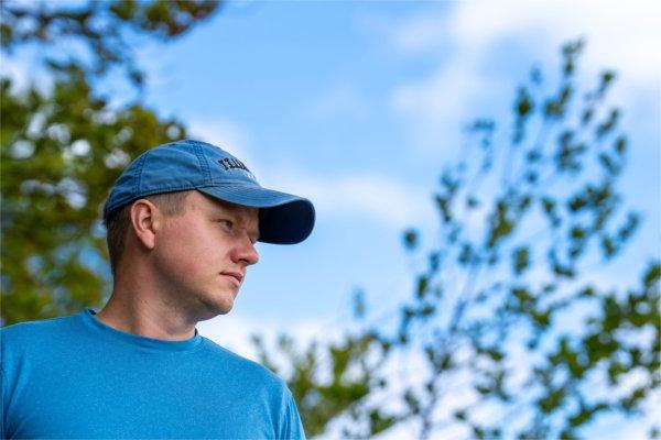 A person wearing a Grand Valley cap looks off into the distance. Trees are in the background.