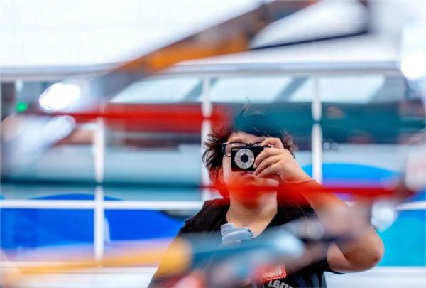  An elementary school student holds a camera in front of their face to photograph a colorful art sculpture. 