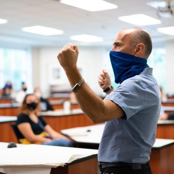 With a face covering, Kurt Ellenberger, professor of music, Meijer Honors College, stands in front of students in the Niemeyer Learning and Living Center.