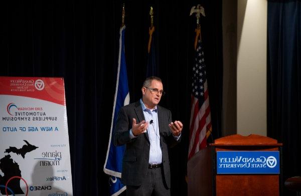 David Leich, executive director of global supply chain for General Motors, speaks next to a podium and in front of several flags on a stage.