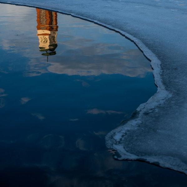 Carillon Tower reflected in Zumberge Pond water, with a curve of ice on the left side.