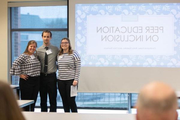 three people standing next to projection screen that reads Peer Education on Inclusion