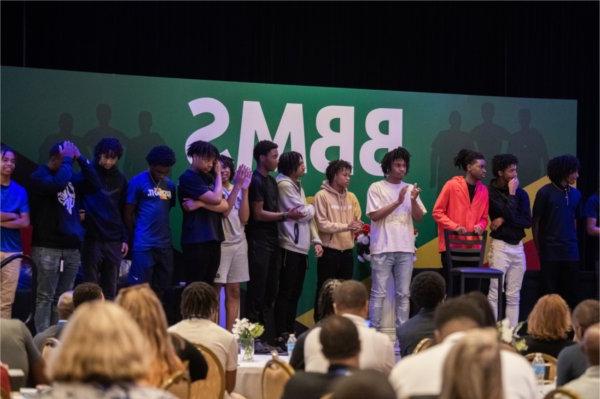 a group of students stands on stage in front of banner, BBMS