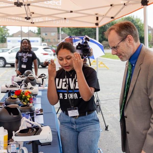 A GVSU student Erika Govea-Garcia explains how to use the VR headset to Mary Free Bed CEO Kent Riddle.