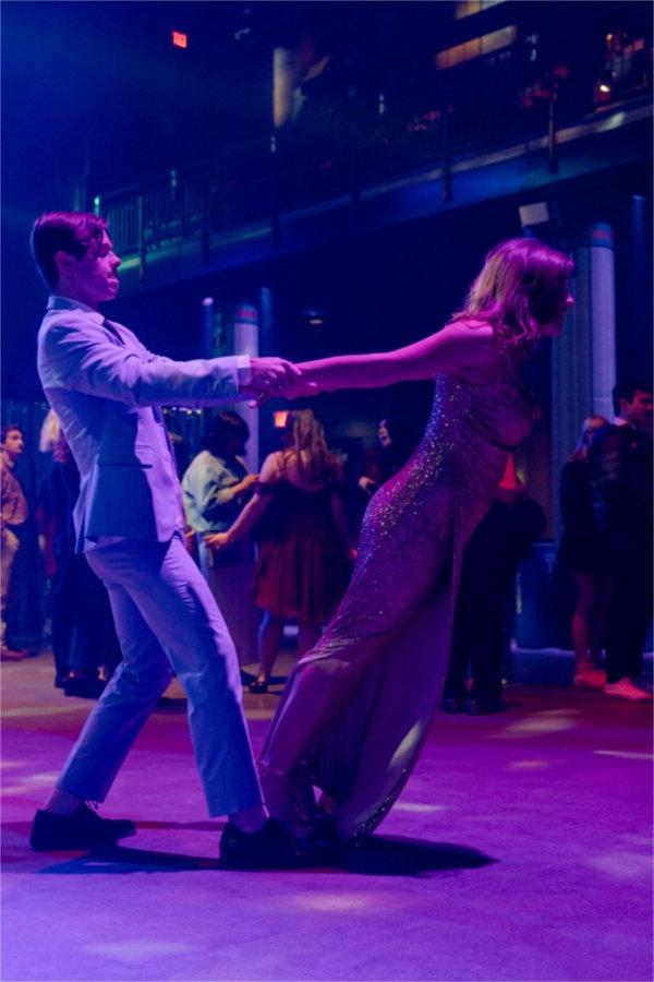 A young man in white dips a young woman wearing a sparkly dress as they dance. 