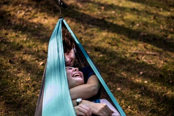 A couple snuggles in a teal hammock while laughing together.