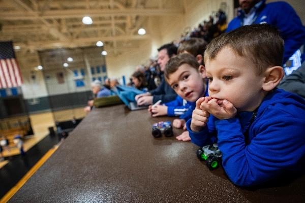  Two small children play with toy cars while watching an event in an arena. 