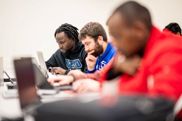 A row of college students work intently on their computers. 