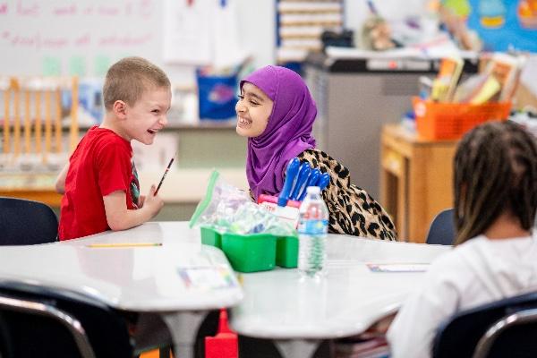  Two children laugh together in an elementary school classroom. 