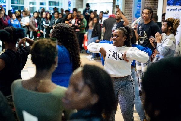 A college student dances in a large group during a black student organization showcase.  