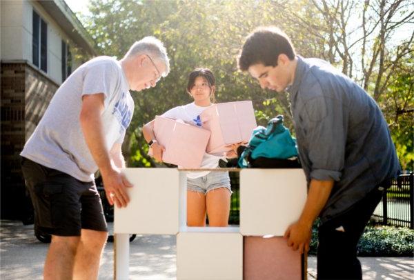 Two people stand on either side of a multi-tiered storage bin. A person behind them holds two storage containers.