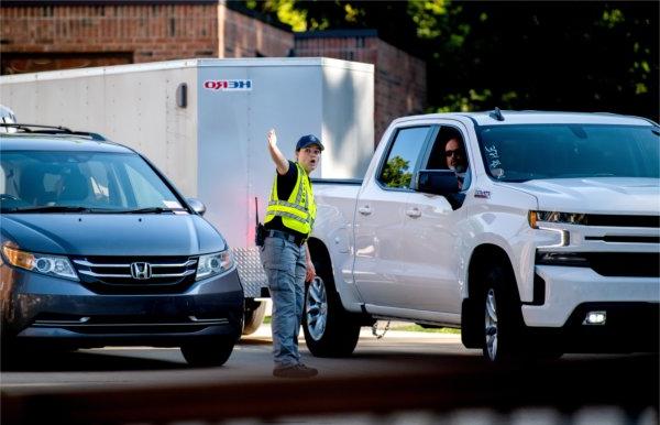 A person wearing a yellow best gestured with their arm to the left while talking to someone driving a pickup truck.