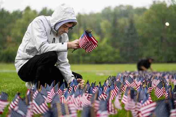 A college student places small American flags into the ground while it's raining.  