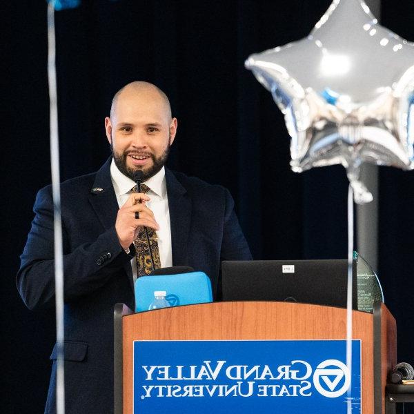 Julian Ramirez-Torres speaks into a microphone from a podium; two balloons frame the podium