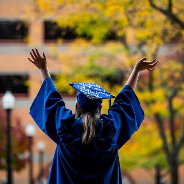 Graduate posing in cap and gown raises her arms in celebration.