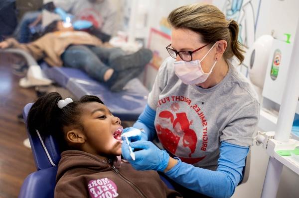 A dental hygienist performs a screening on a girl's teeth.