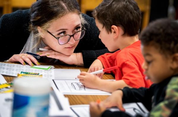 Elementary students with markers work with a GVSU student on an activity.